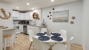 Een moderne keuken met witte kasten, een magnetron en een eethoek met een ronde tafel en witte stoelen.