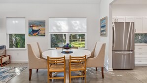 Une cuisine moderne avec des meubles blancs, un réfrigérateur en acier inoxydable et un coin repas comprenant une table ronde et des chaises.
