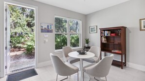 A modern room with a dining table and chairs, a bookshelf, and large windows offering a view of greenery. - American Beach Retreat - Hosted by Moore AI Rentals (Fernandina Beach)