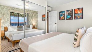 Una habitación de hotel con dos camas, un ventanal grande, una puerta y tres cuadros enmarcados en la pared.