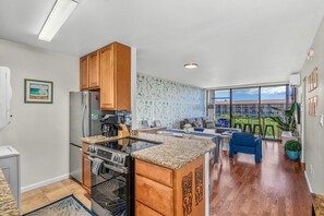 Une cuisine moderne dotée d’un îlot central, de meubles en bois et d’une grande fenêtre donnant sur un balcon.