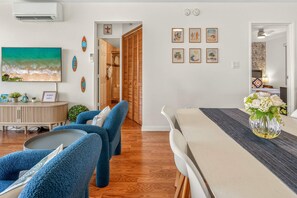 A modern living room with a large painting, a dining area with a table and chairs, and a hallway leading to a bedroom.