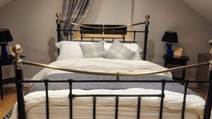 Een slaapkamer met een bed, een zwart metalen frame, witte beddengoed en een raam met gordijnen.