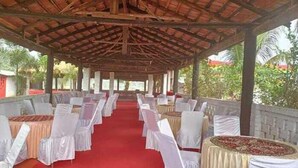 An outdoor covered area with rows of tables and chairs, a red carpet, and a view of greenery. - Green Point Hotels and Resorts (Angul)