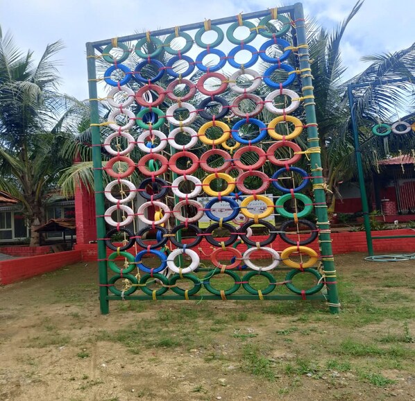 A playground structure made of interlocking tires in various colors, surrounded by palm trees and a red building. - Green Point Hotels and Resorts (Angul)