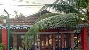 A building with a red brick facade, a tiled roof, and a covered entrance with a palm tree. - Green Point Hotels and Resorts (Angul)