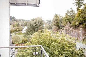 Un balcon donnant sur un paysage rural, avec des arbres et un bâtiment blanc.