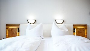 A double bed with white bedding, two bedside tables with illuminated lamps, and a wooden headboard. - Comfortable and versatile room -perfect for relaxation, work and exchange (Winterberg)
