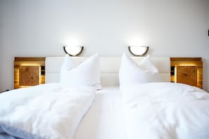 A double bed with white bedding, two bedside tables with illuminated lamps, and a wooden headboard.