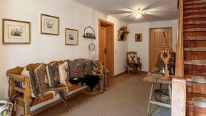 Un interior rústico con un sofá de madera decorado con cojines de motivos animales, una mesa de madera con una cesta tejida y una puerta de madera con una manija decorativa.