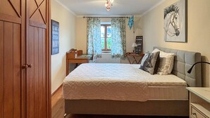 Un dormitorio con cama, escritorio, silla y ventana con cortinas.