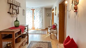 Una sala acogedora con una mesa de madera, un florero verde, un tapete estampado y un sillón rojo.