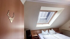 A bedroom with a skylight, a bed with white bedding, a wooden headboard, and a wall-mounted deer head decoration. - A comfortable and versatile room—perfect for relaxation, work, and socializing (Winterberg)