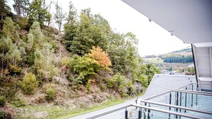 Um edifício moderno com varanda de vidro com vista para uma colina arborizada e paisagem campestre.