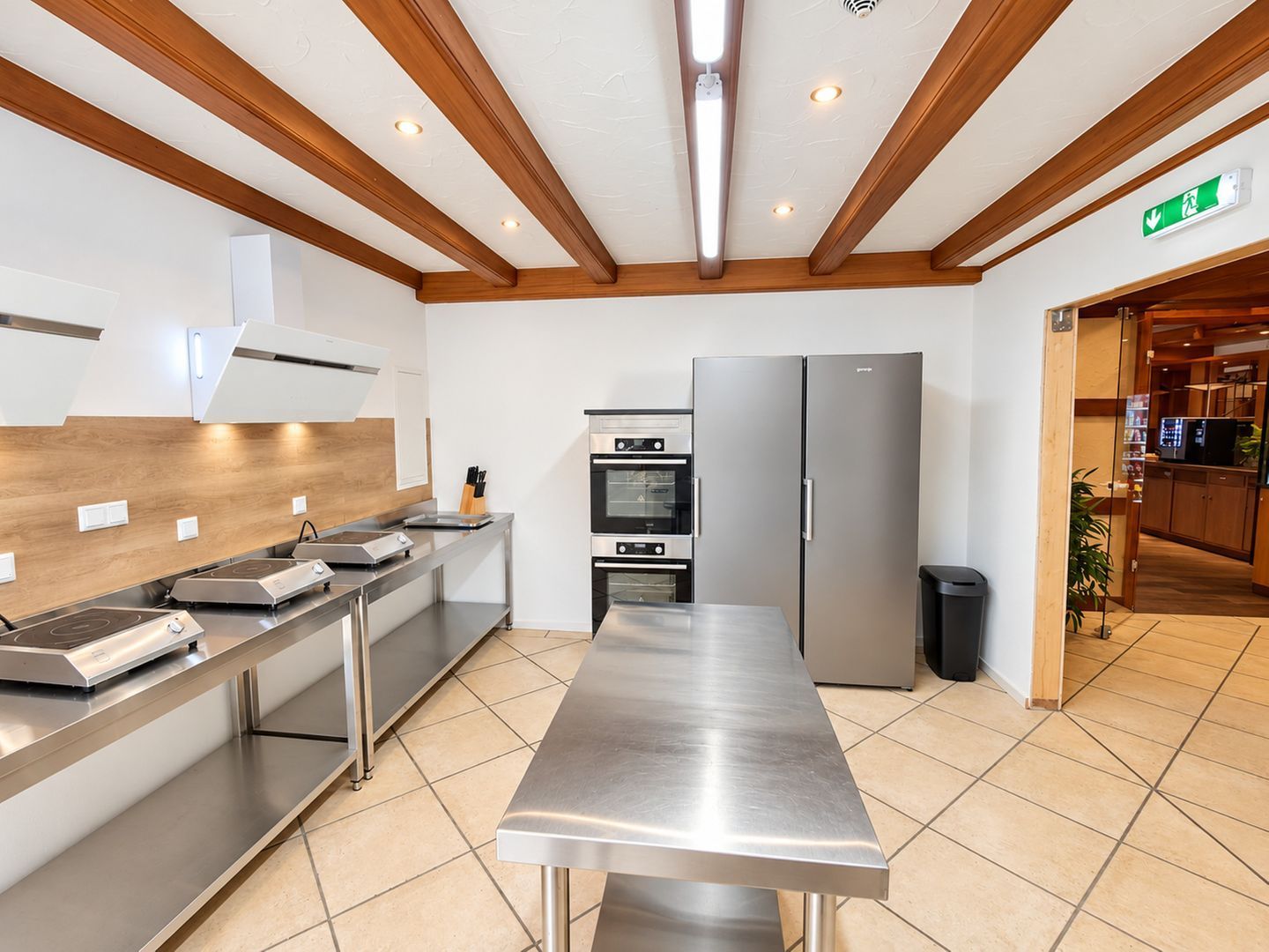 A modern kitchen with stainless steel appliances, wooden beams, and a tiled floor.