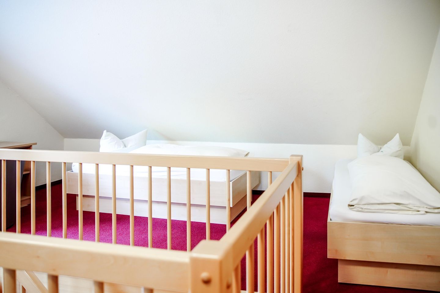 A room with a crib, a bed, and a nightstand.
