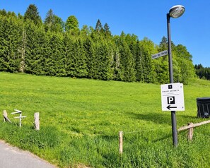 A parking sign with directional arrows, a fence, and a grassy field with trees in the background. - Comfortable and versatile room -perfect for relaxation, work and exchange (Winterberg)