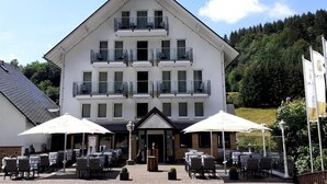A multi-story building with balconies, outdoor seating, and flags. - Comfortable and versatile room -perfect for relaxation, work and exchange (Winterberg)