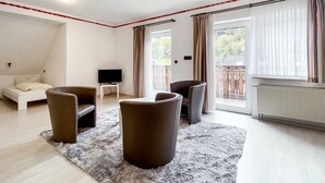 A modern living room with a sofa, two armchairs, a TV on a stand, a fluffy rug, and a large window with curtains. - Comfortable and versatile room -perfect for relaxation, work and exchange (Winterberg)