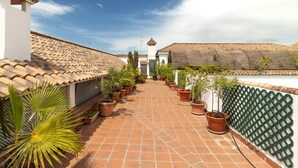Un patio con techo de tejas de terracota, plantas en macetas y una cerca de celosía verde.