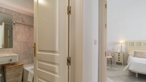 Una habitación de hotel con baño, cama, mesita de noche y velador.