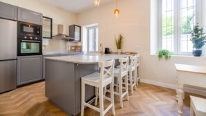 A modern kitchen with stainless steel appliances, a central island with bar stools, and a window with plants.