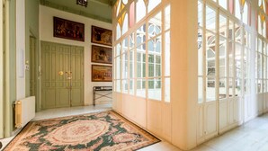 A spacious room with a large ornate window, a green door, and a patterned rug.