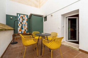 A patio with yellow chairs and a table, a tiled floor, a wall with a colorful checkered pattern, and a door with a window. - La Morada del Pintor (Cordoba)