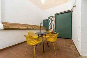A small outdoor seating area with yellow chairs and a table, a tiled floor, and a green door with a colorful tile design. - La Morada del Pintor (Cordoba)