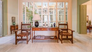 A room with a large bay window, a wooden desk with two chairs, a lamp, and a bookshelf.