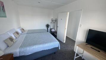 A bedroom with two beds, a TV, a desk, and a door leading to another room.