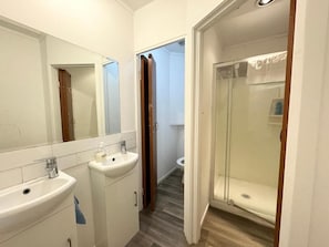 A bathroom with two sinks, a mirror, and a glass-enclosed shower. - Rainbow Motel & Guest House (Tauranga)