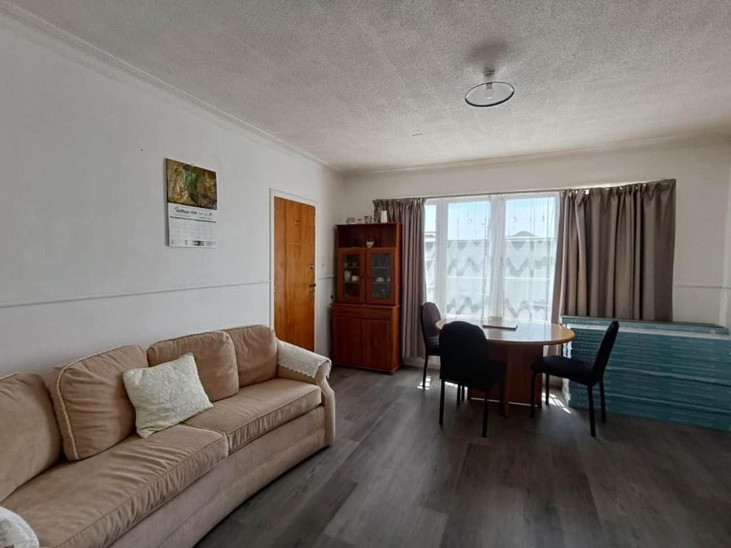 A living room with a sofa, a dining table with chairs, a wooden cabinet, and a window with curtains.