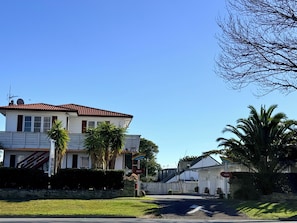 A two-story residential house with a red roof, white siding, and a front yard with palm trees.