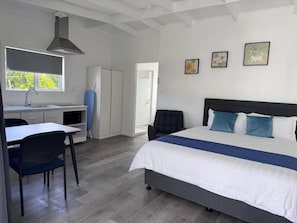 A bedroom with a bed, a desk, and a chair. There is a window with a view of trees. - Rainbow Motel & Guest House (Tauranga)