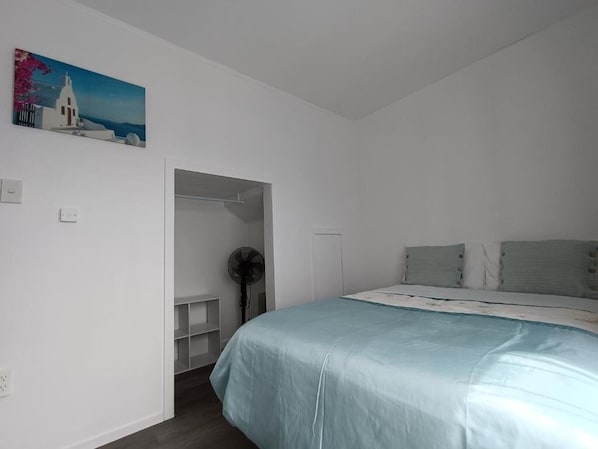 A bedroom with a bed, a fan, and a painting on the wall.