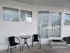 A balcony with two chairs and a small table, large windows with curtains, and a concrete ledge.