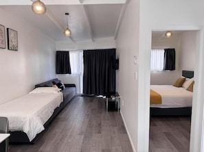 A hotel room with two beds, a sofa, a TV, and a desk. - Rainbow Motel & Guest House (Tauranga)