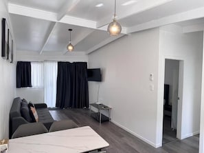A modern living room with a sofa, a coffee table, and a flat-screen TV. - Rainbow Motel & Guest House (Tauranga)