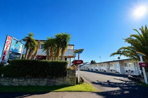 A motel with a signboard, palm trees, and a clear sky. - Rainbow Motel & Guest House (Tauranga)