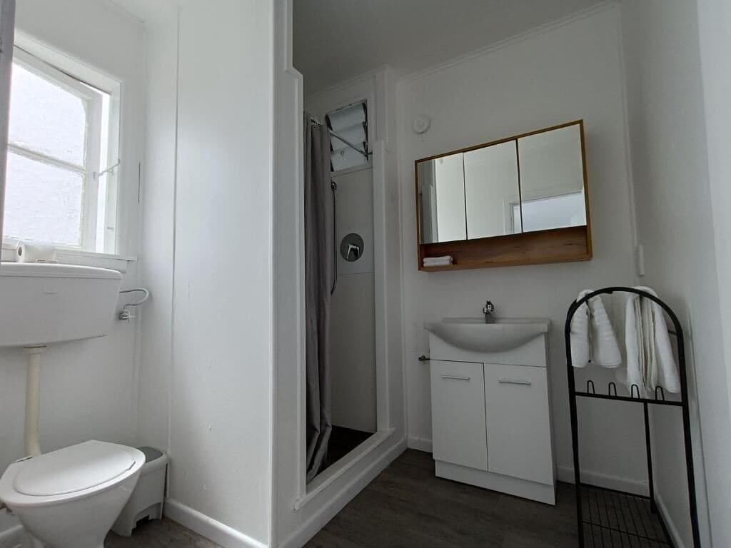 A bathroom with a toilet, sink, mirror, and shower.