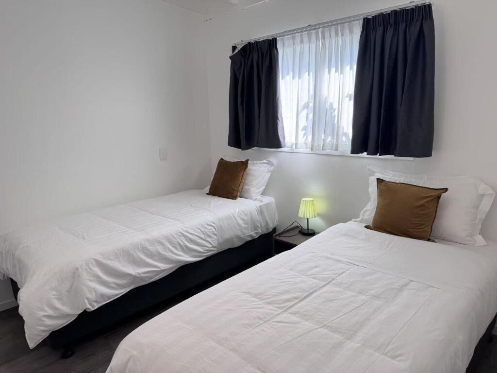 Une chambre avec deux lits simples, une fenêtre avec des rideaux et une lampe de chevet.