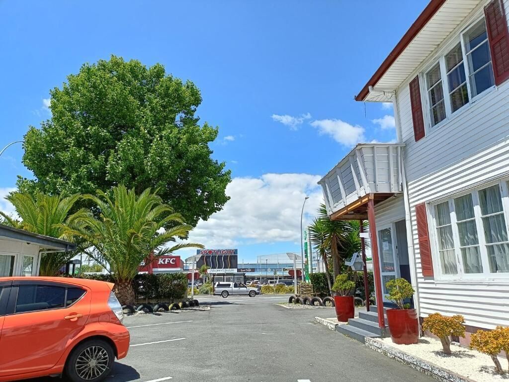 Vista de la calle con un restaurante KFC, un coche aparcado y un edificio con porche.