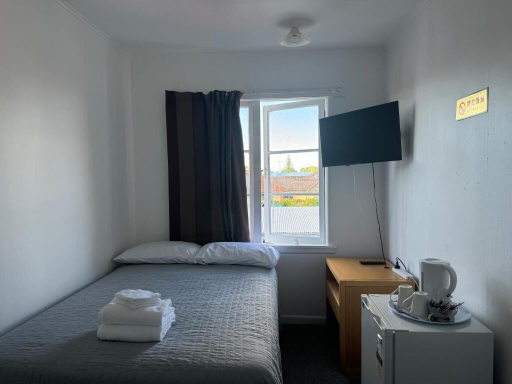 Une chambre d’hôtel avec un lit, un bureau, une télévision et une fenêtre avec des rideaux.