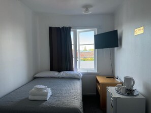A hotel room with a bed, a desk, a television, and a window with curtains. - Rainbow Motel & Guest House (Tauranga)