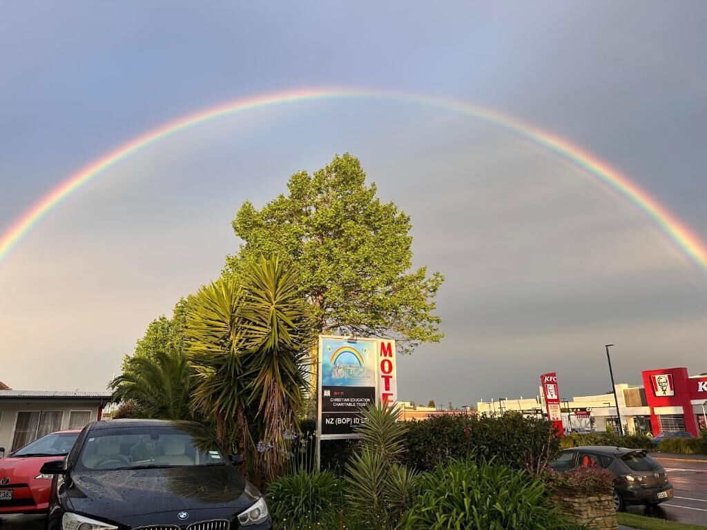 A motel with a signboard, a tree, and a rainbow in the background.