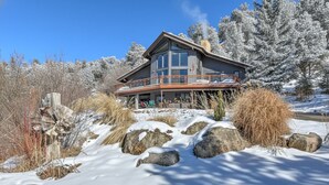 Une grande maison moderne dotée d’un balcon, entourée d’arbres et de rochers couverts de neige.