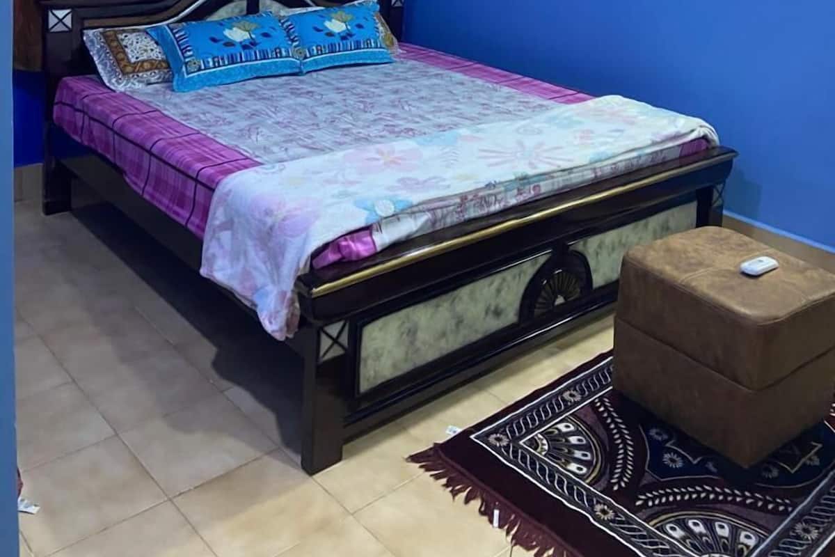 A bedroom with a bed, a ceiling fan, and a small ottoman.