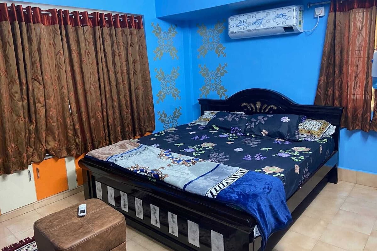 A bedroom with a bed, curtains, an air conditioning unit, and a small table.