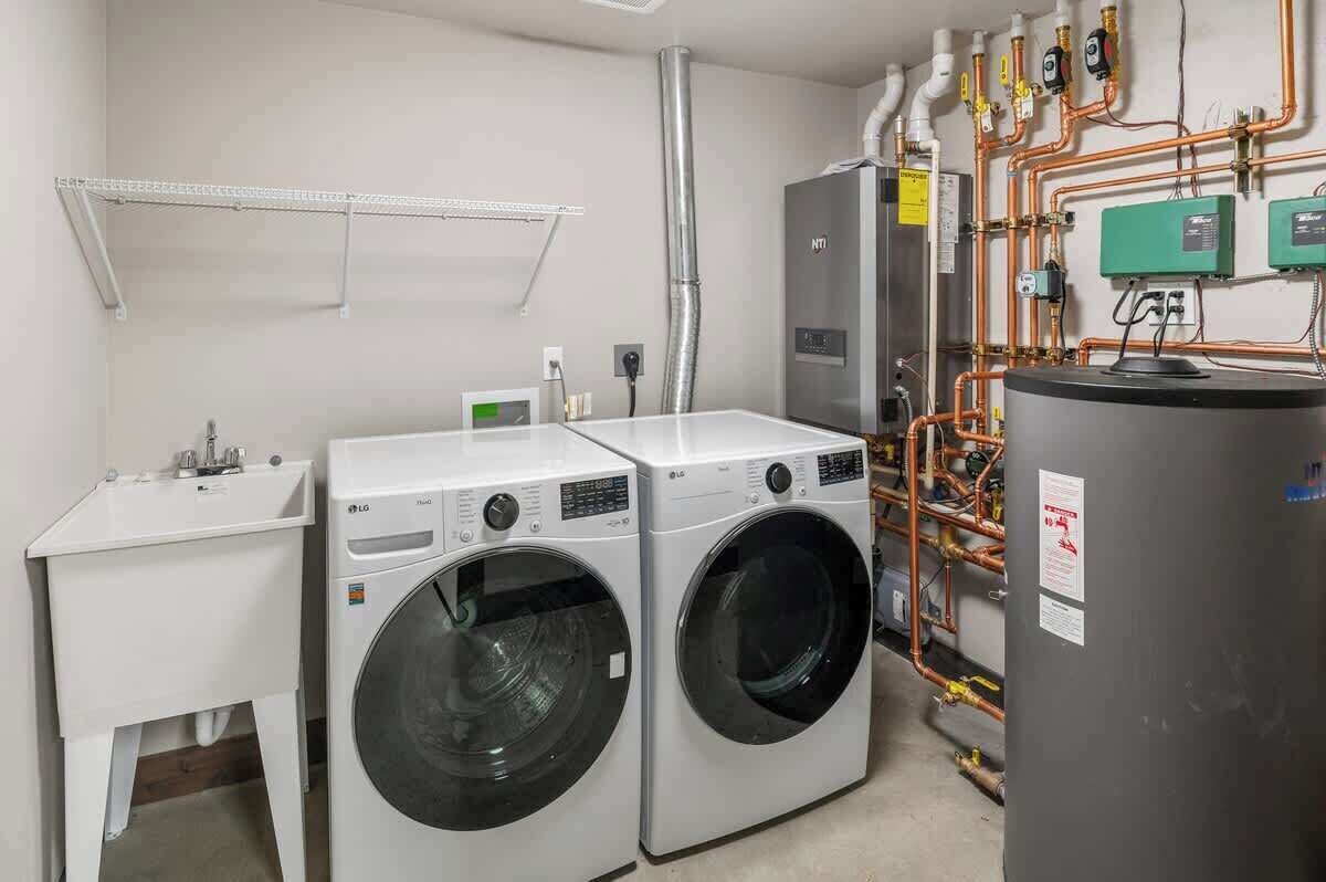 A laundry room with two LG front-loading washers, a white sink, and a large water heater.